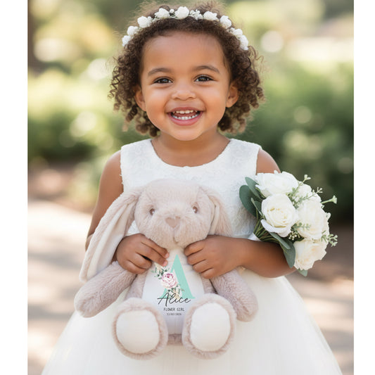 Young girl in a white dress holding a plush bunny and bouquet of flowers outdoors.