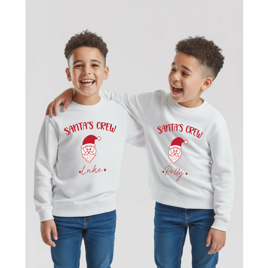Two children wearing white sweatshirts with 'Santa's Crew' text and a Santa face design with their names below the Santa Face design