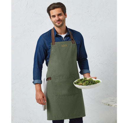 Man wearing a Moss Green Apron with Leather Accents. Apron has initials embroidered on the top middle chest