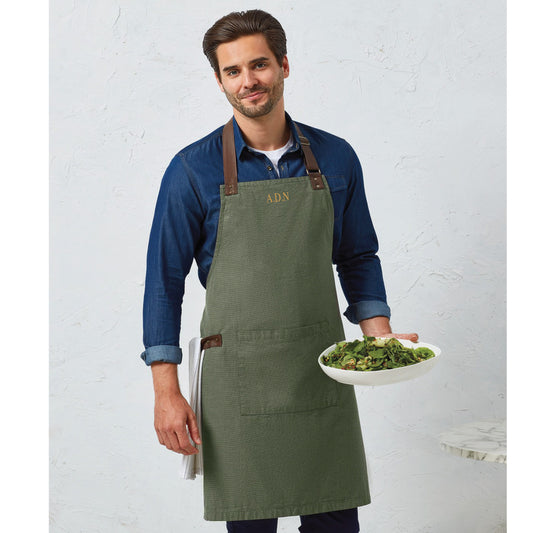 Man wearing a Moss Green Apron with Leather Accents. Apron has initials embroidered on the top middle chest