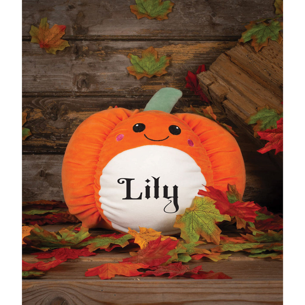 Pumpkin-shaped plush toy with a face and name 'Lily' on a wooden background with fall leaves.
