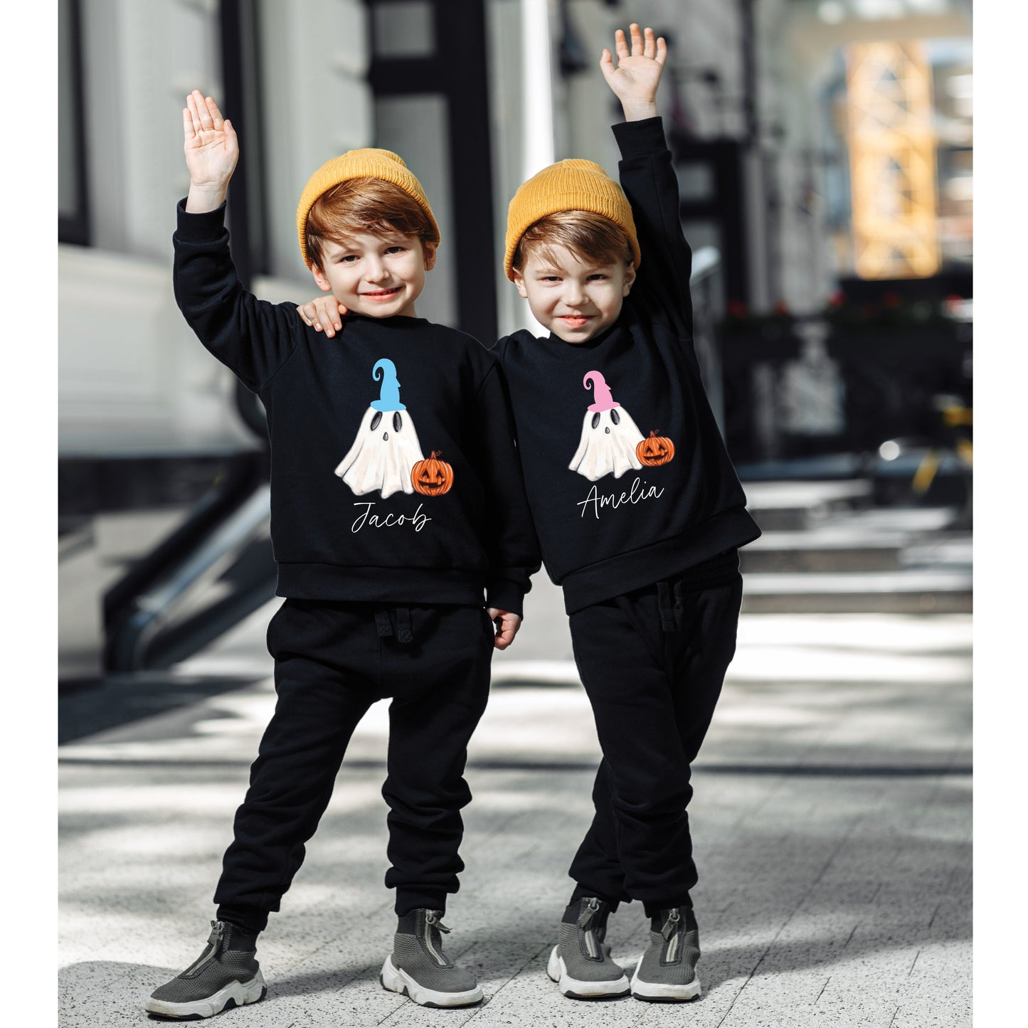 Two children wearing black sweatshirts with ghost designs and names, standing on a city street.