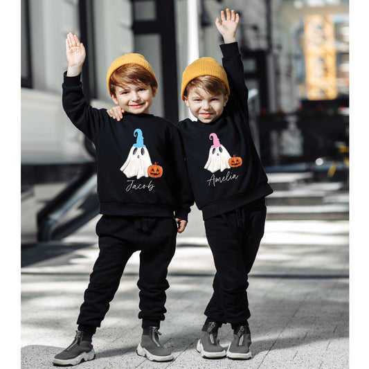 Two children wearing black sweatshirts with ghost designs and names, standing on a city street.