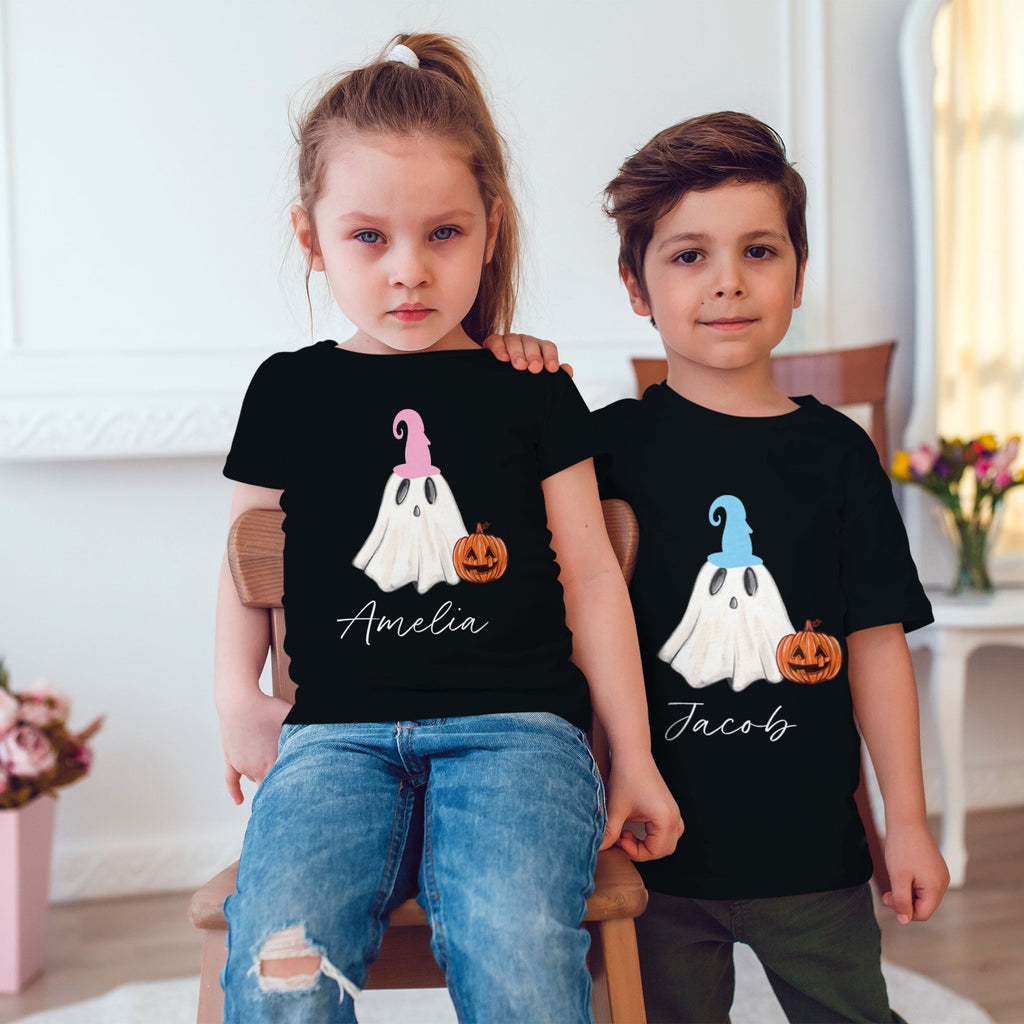 Two children wearing black t-shirts with ghost and pumpkin designs, sitting on a chair.